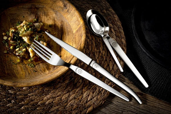 several Laguiole heritage flatware items placed above a wooden bowl